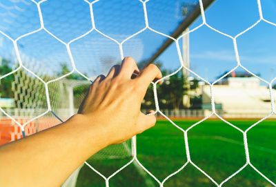 Close-up of hand on soccer field seen through chainlink fence