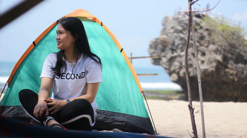 Young woman looking away while sitting in tent at beach