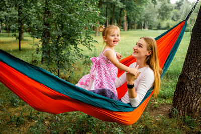 Young mother and cute little daughter relaxing together and smiling sitting in a hammock