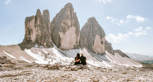 Rear view of couple sitting on rock against mountain