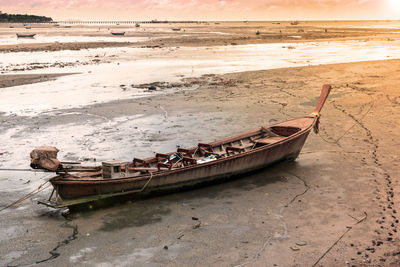 Boat moored on beach against sky during sunset