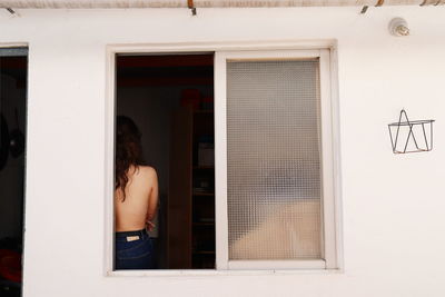 Rear view of shirtless woman standing by window