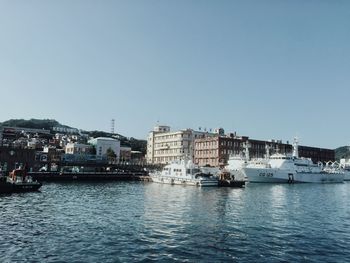 Sailboats in harbor by buildings against clear sky