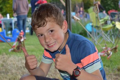 Portrait of boy showing thumbs up while sitting on grassy field at park