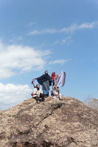 Low angle view of people sitting on rock against sky