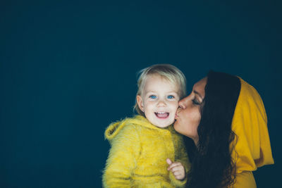 Woman kissing daughter against black background