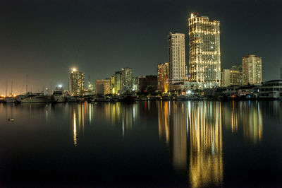 Illuminated buildings by river against sky at night