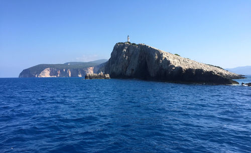 Lighthouse on cliff by ocean against clear blue sky