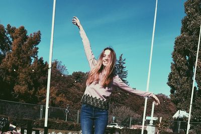 Smiling young woman standing on street against sky