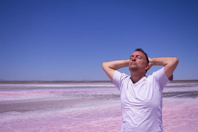 Mature man with eyes closed standing at beach against clear blue sky