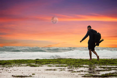 Full length of man walking at beach against sky during sunset