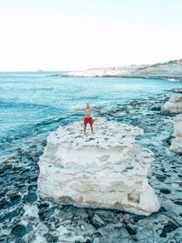 Full length of man on rock at beach against sky