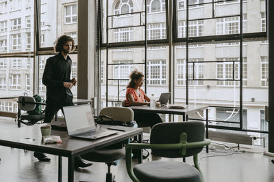 Female entrepreneur using laptop while male colleague walking by at coworking space