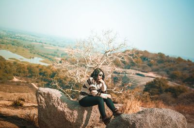 Man sitting on rock against sky