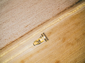 Aerial view of powerful fast yellow vehicle working on field cultivating harvest of wheat