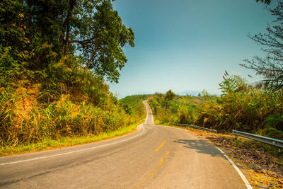 Country road amidst trees against sky