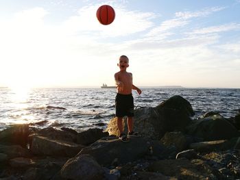 Full length of shirtless boy playing with ball at beach against sky