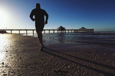 Silhouette man walking on beach against clear sky