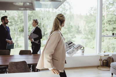 Female with magazine looking through window while partner consulting real estate agent at new property