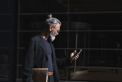 Hipster businessman with file using smart phone by building