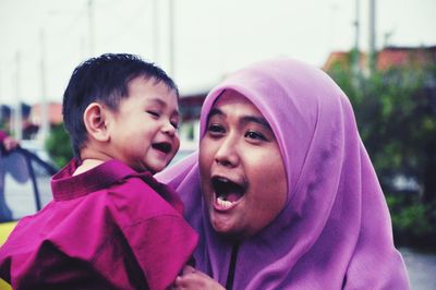 Happy mother shouting while carrying boy against sky