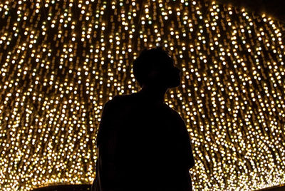 Rear view of silhouette man standing against illuminated lights