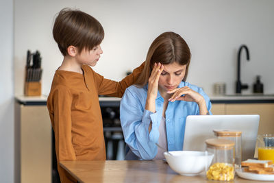 Smiling young woman using phone while sitting on table at home