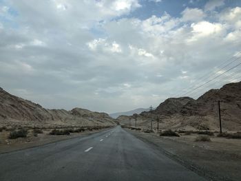 Empty road leading towards mountains against cloudy sky