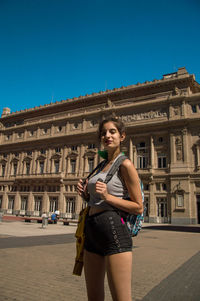 Full length of young woman using phone in city against clear sky