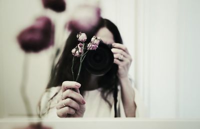 Woman photographing dry flowers while reflecting in mirror