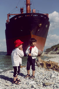 Two fashionable baby boys stand next to a large rio ship that ran aground off novorossiysk