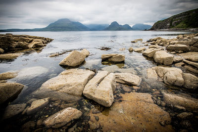 Rocks on shore by lake against sky