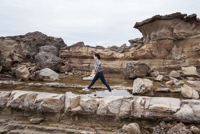 Traveling asian female standing on rock on background of waving sea on cloudy day on east coast