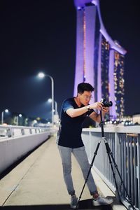 Full length of young man photographing on bridge at night