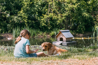 Friendship of animals and children. caucasian girl sits on of a pond and plays with  puppy, labrador
