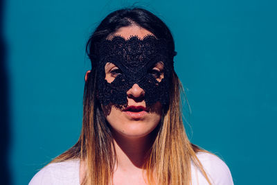 Portrait of young woman wearing mask against blue background