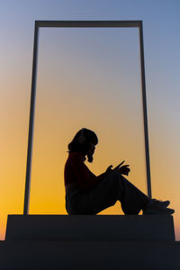 Low angle view of silhouette man sitting against sky during sunset