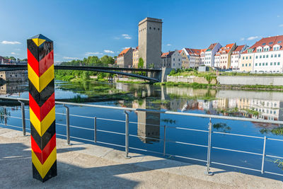 Multi colored flag on railing by river against buildings in city