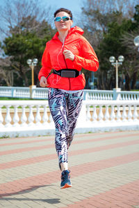 A full-length athletic woman in bright clothes is jogging in the morning around the city