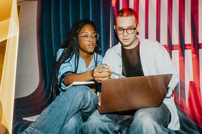 Female business professional assisting male colleague using laptop at office