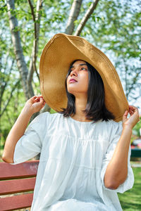 Young woman looking away while standing against tree