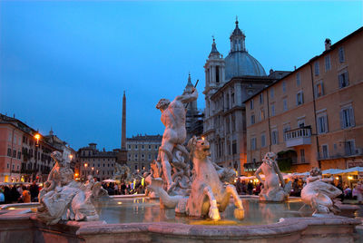 Fountain of neptune by old buildings against sky at dusk