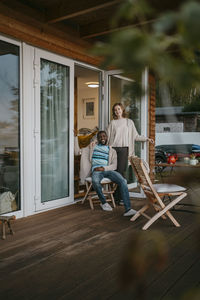 Young woman standing by man sitting on chair at porch outside house