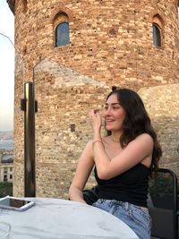 Young woman using mobile phone while sitting on brick wall