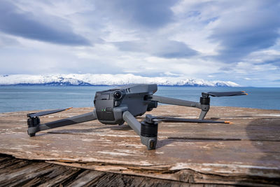 Close-up of drone on wooden bench with sea in background against cloudy sky