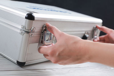 Cropped hands opening suitcase over table
