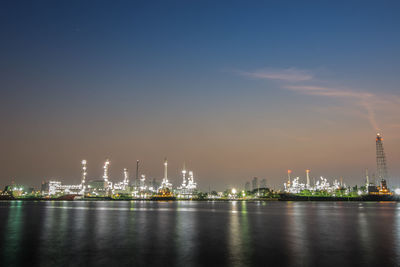 Illuminated city by river against sky at night