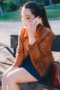 Smiling young woman listening over phone while sitting on bench