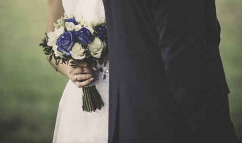 Midsection of bride with bridegroom holding bouquet