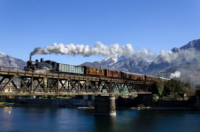 Smoke emitting from train on bridge over river in city
